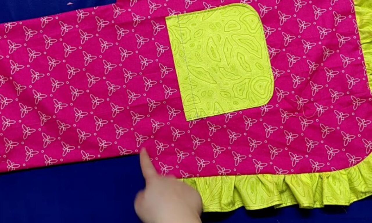 a bright pink fabric with a repeating white butterfly pattern. On top of the fabric, there is a square patch in a vibrant yellow-green color, featuring an intricate stitched design. The bottom edge of the fabric has a ruffled trim in the same yellow-green color, matching the square patch.