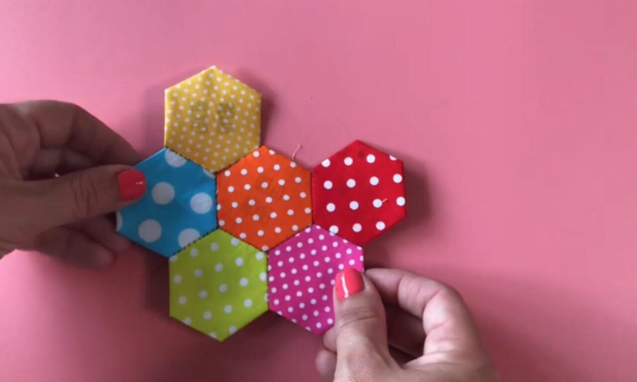 A pair of hands holding a colorful, handmade hexagon patchwork from various fabrics with polka dots, showcasing a vibrant mix of patterns and colors.