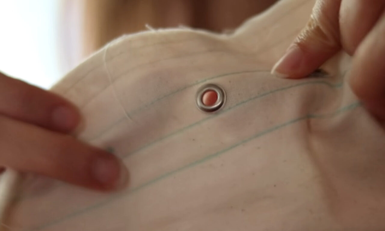 a person's hands adjusting the collar of a white, striped shirt with a single red and silver button.