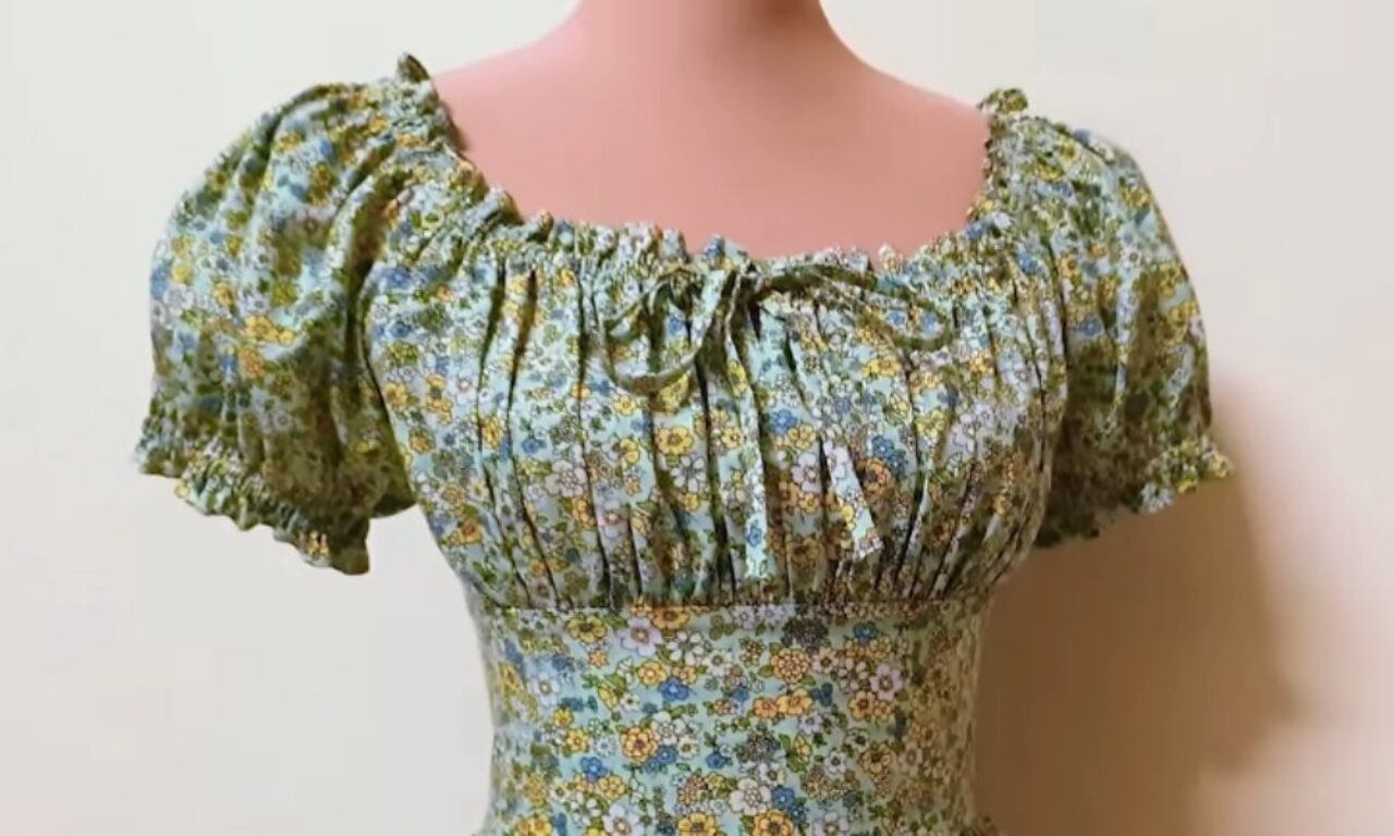 Close-up of a green, blue, yellow, and white floral dress with puffed sleeves and a square neckline on a pale pink mannequin torso against an off-white background.