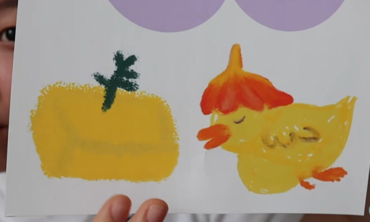 A hand-drawn picture on white paper shows a yellow chick with an orange beak and feet, and a red-orange tuft on its head. The chick has its eyes closed and appears to be walking or dancing. To the left of the chick is a yellow rectangular shape with a green leafy top, resembling a stylized pumpkin or squash. A person is partially visible behind the paper, holding it up to display the artwork.