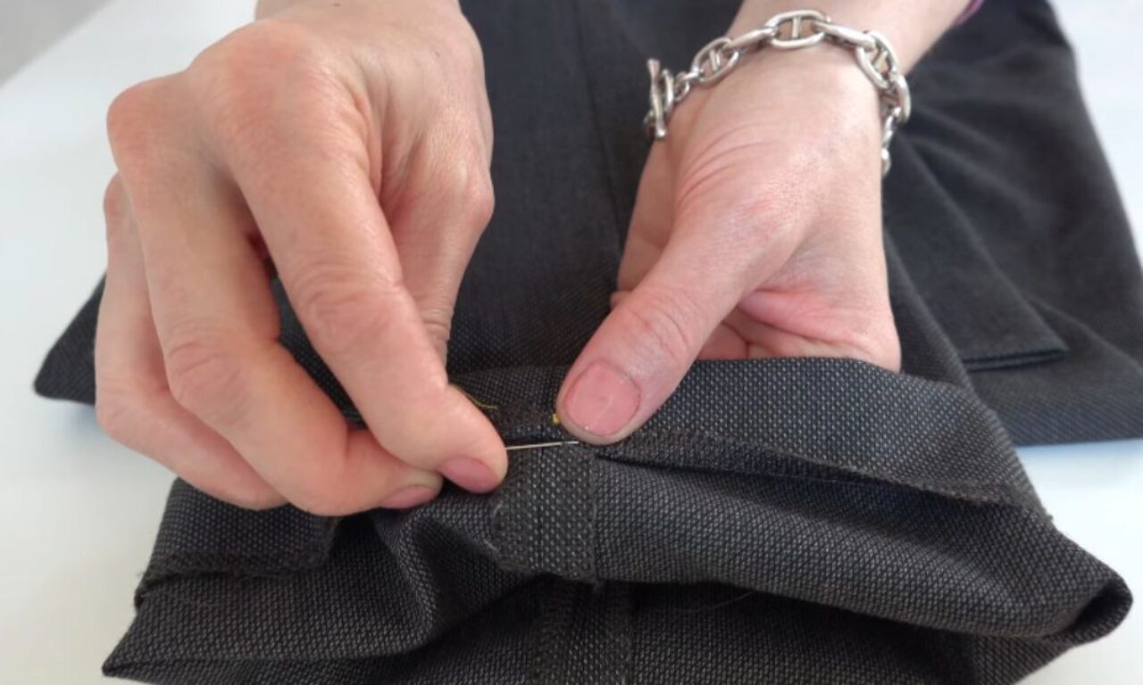 Hands sewing dark fabric with a needle and yellow thread.