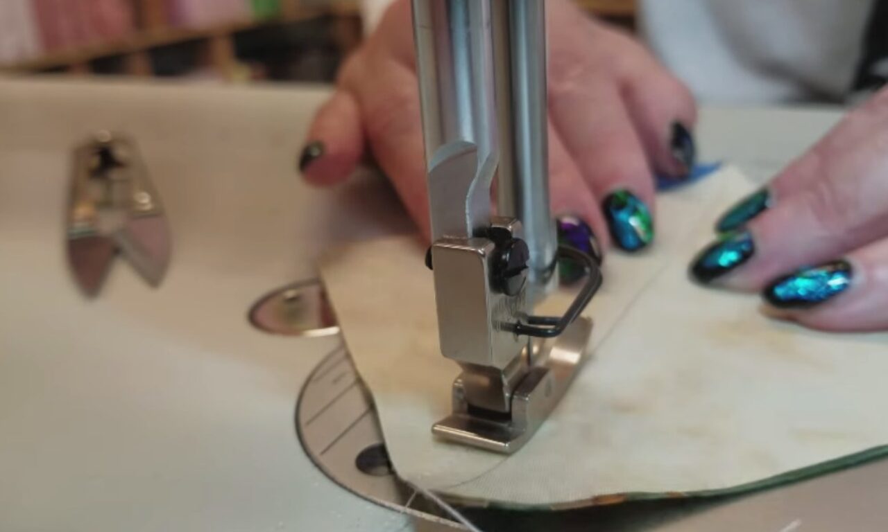 Stitching fabric on a sewing machine, hands visible guiding the material under the needle.