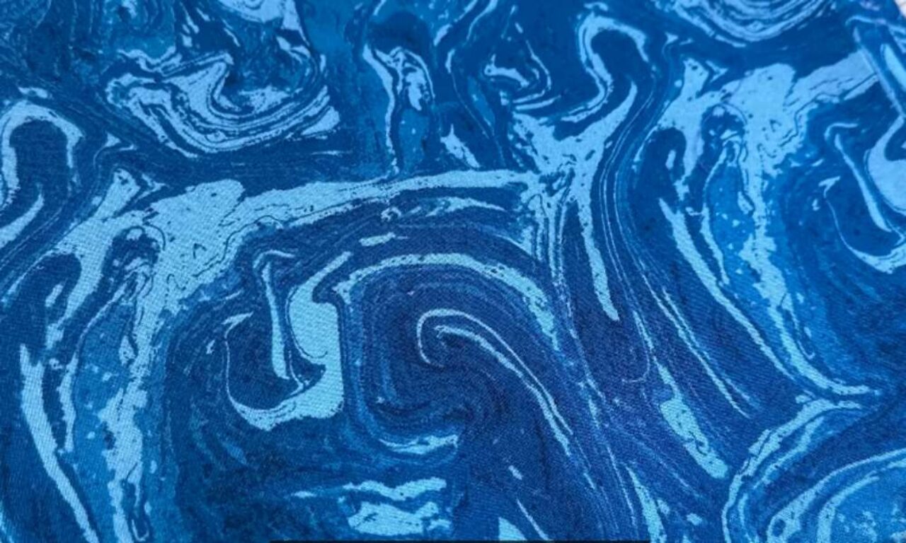 Abstract marble-like pattern of swirling deep blues, light blues, and white, resembling fluid ocean currents.