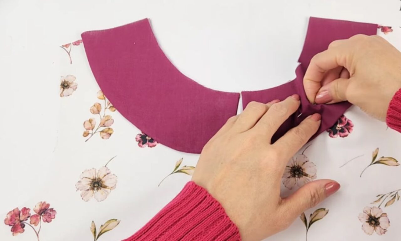 stitching a piece of purple fabric onto a white floral-patterned garment, creating a new collar.