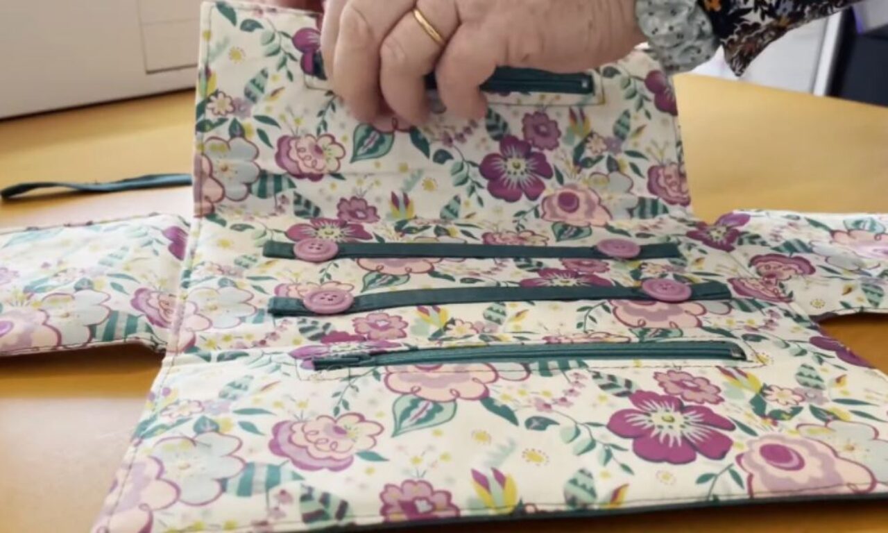 A floral fabric organizer in purple, pink, and green is open, showing straps with purple buttons and zippered pockets inside.