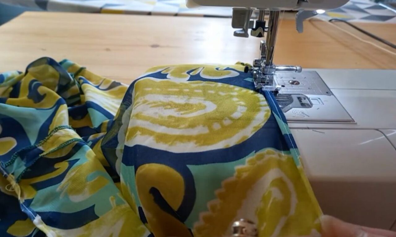 Sewing machine hemming a lightweight, patterned fabric with swirls of yellow, blue, and light blue.