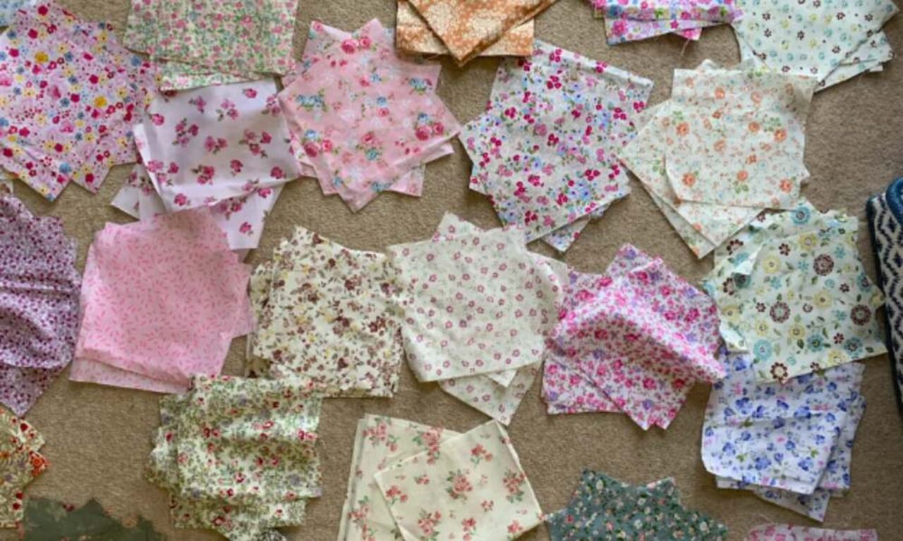 many square pieces of fabric with different floral prints scattered on a beige carpet. The fabrics are mostly light colored with pink, blue, yellow, and green flower patterns.