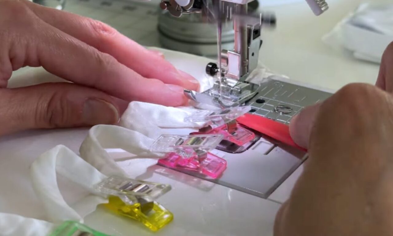 a person using a sewing machine with various colored sewing clips attached to white fabric, guiding it through the machine.