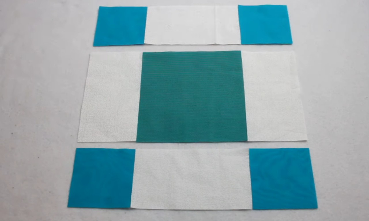 Three pieced fabric units for a quilt block, arranged horizontally. Two identical units consist of a white center strip with turquoise squares sewn to each end. A third, central unit consists of a large teal square with white strips sewn to the sides.