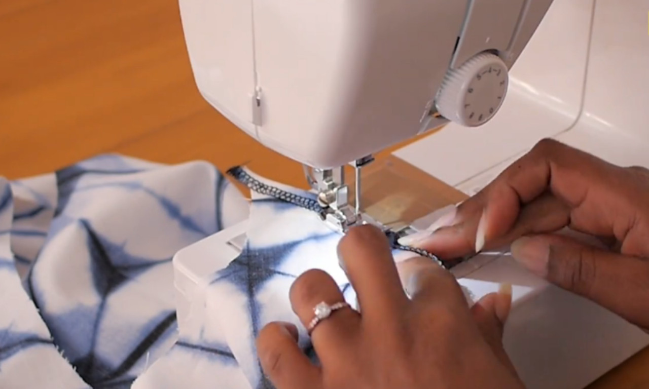 a close-up of hands sewing a ruffled fabric on a sewing machine.