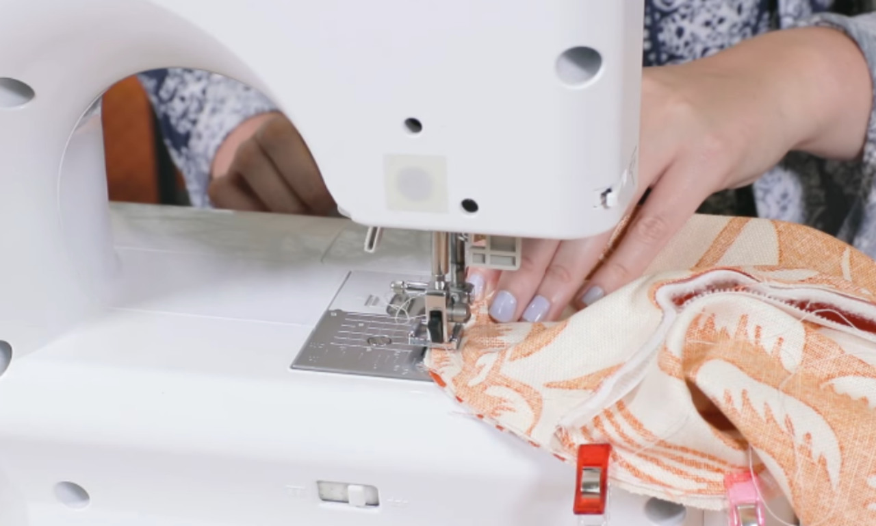 a person sewing fabric on a sewing machine. The fabric has a pattern with orange and white designs.