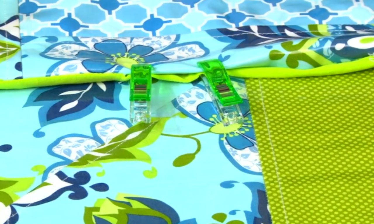 a vibrant fabric featuring a floral pattern with shades of blue and green. Two green clothespins hold the fabric in place.