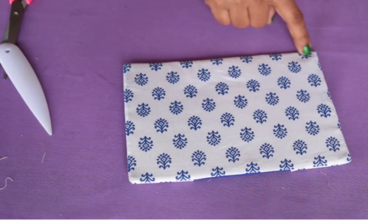 a hand holding a pair of scissors above a piece of fabric with a blue floral pattern.