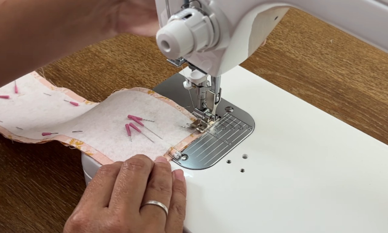 a person's hands guiding a piece of pinned fabric through a sewing machine.