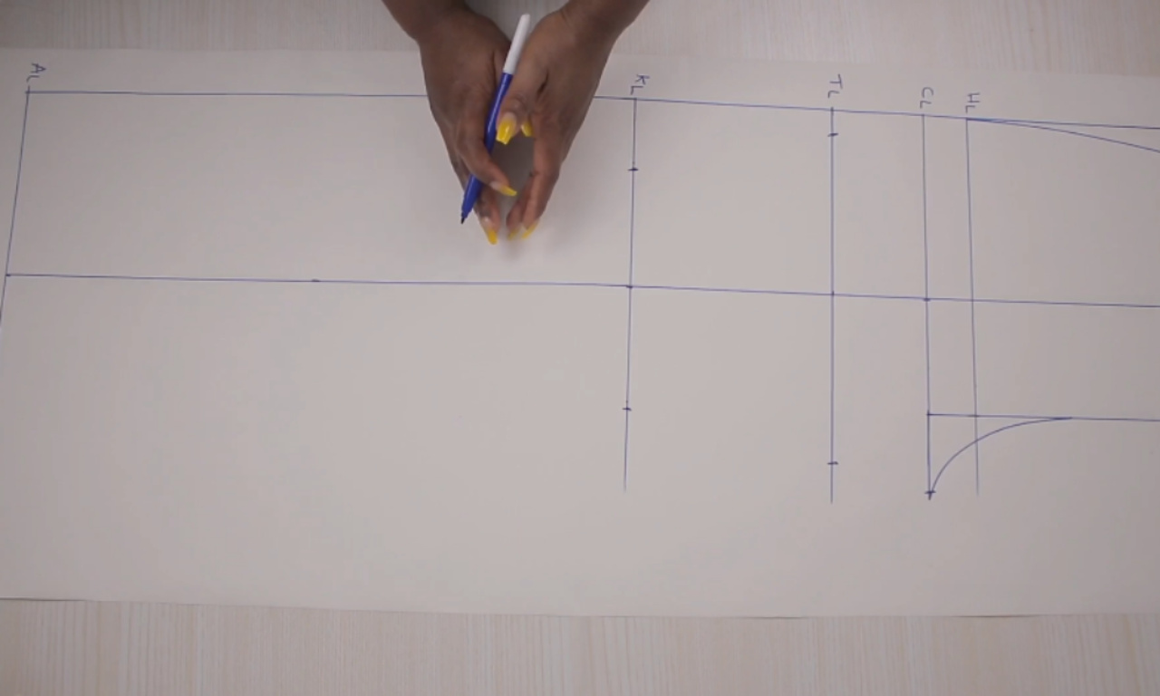 a blue marker over a large white sheet of paper. Blue lines are drawn on the paper, forming a garment pattern, likely for pants or trousers. The pattern features a grid of vertical and horizontal lines, with labels along the top including 'AU', 'KL' (Knee Line), 'TL' (Thigh Line), 'CL' (Crotch Line), and 'HL' (Hip Line). Two distinct curved lines, resembling the crotch and inner thigh of a pants pattern, are visible on the right side.