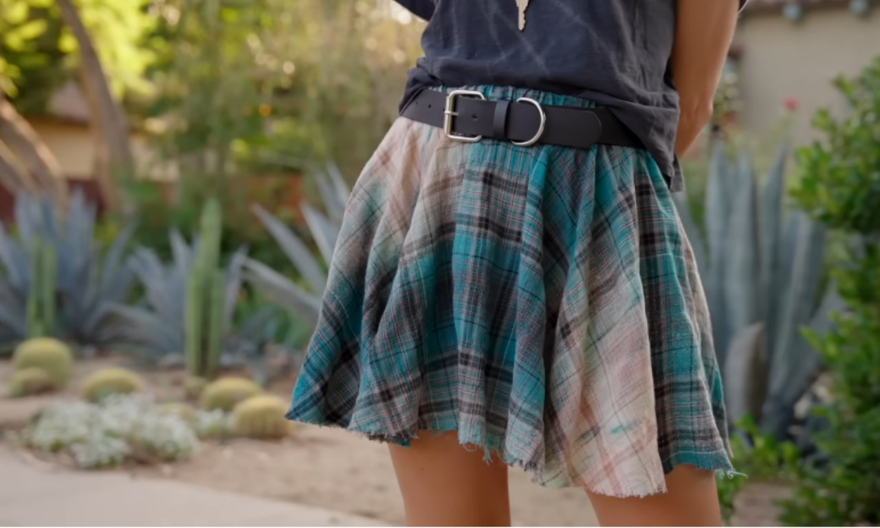 A person wearing a plaid skirt made from a repurposed flannel shirt, standing in a desert garden with cacti and other plants in the background.