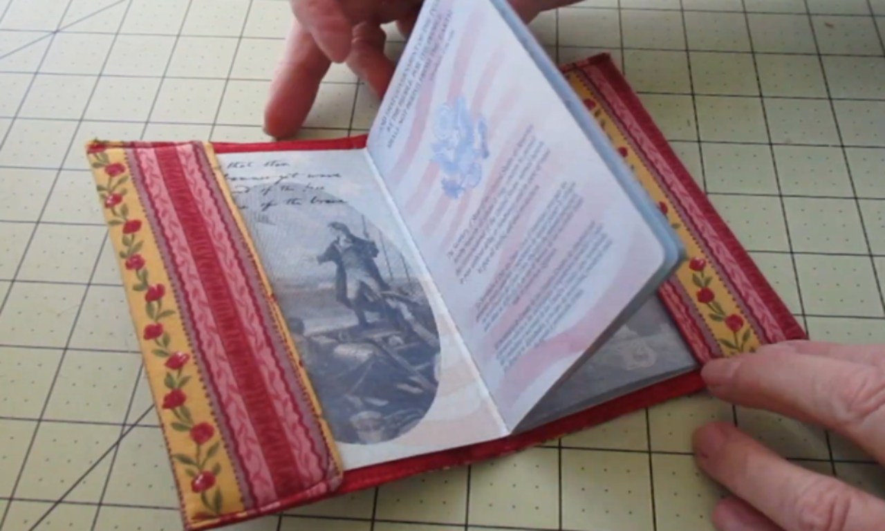 a person's hands holding an open US passport nestled inside a custom-made fabric cover. The cover is red, with interior flaps featuring a yellow floral and red striped pattern.