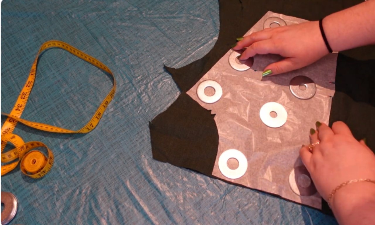 pattern pieces for a Renaissance-inspired bodice. The pieces are made of white paper and are arranged on a textured blue fabric. A measuring tape and seam ripper.
