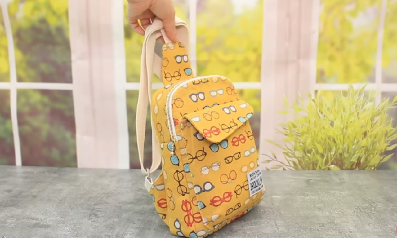 a hand holding up the finished bag, which is yellow and has a print of various colorful eyeglasses.