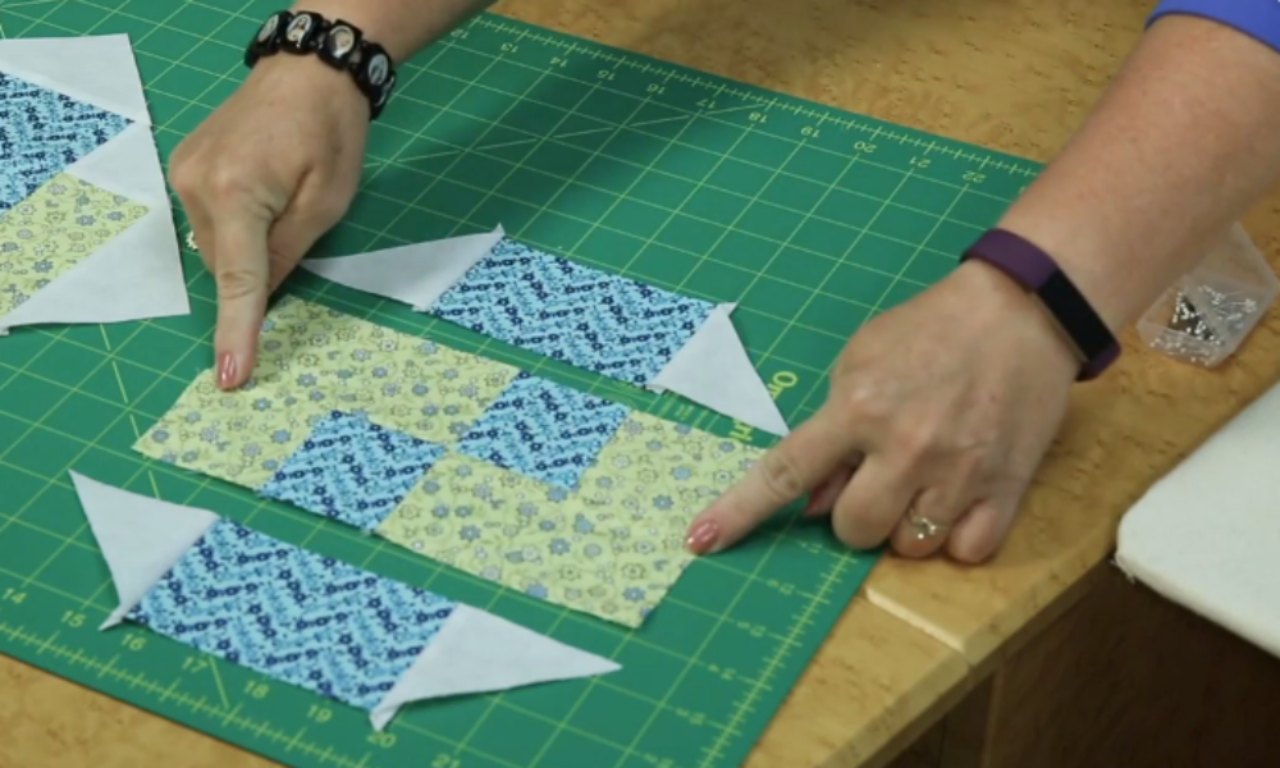 A quilter demonstrating how to assemble the three diagonal rows of a Glad All Over quilt block. The rows are laid out on a green cutting mat before being sewn together.