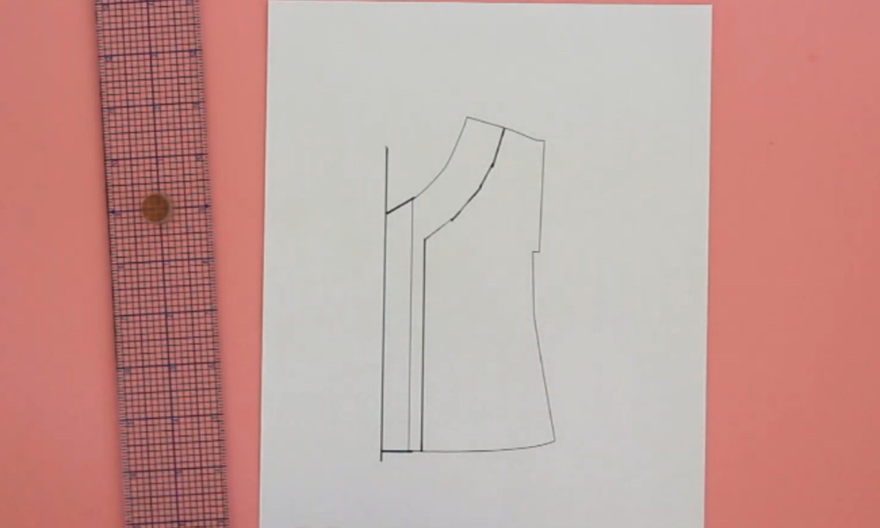 A diagram on white paper showing a sewing pattern alteration for adding a button placket to a shirt, with a clear gridded ruler lying next to it on a pink surface.