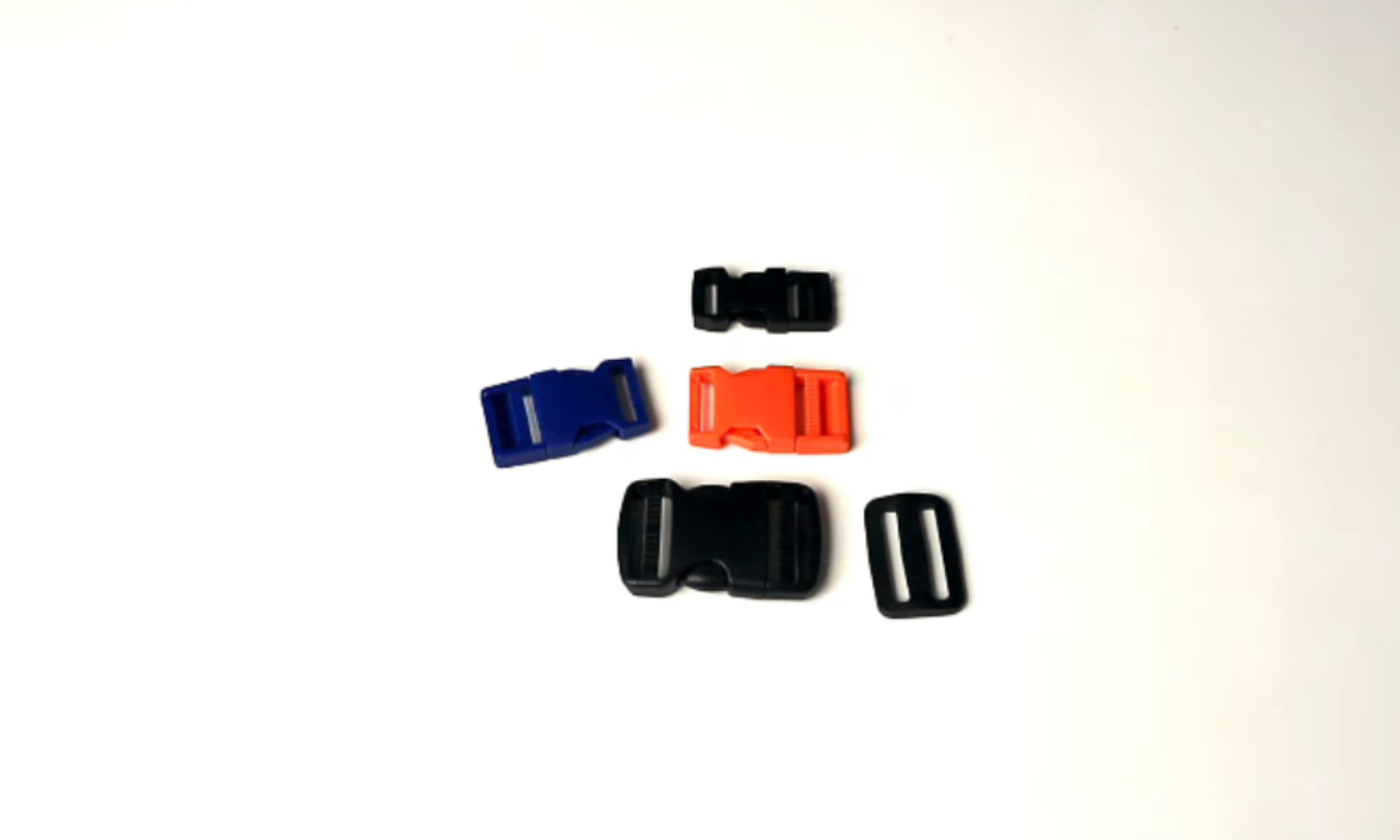 An assortment of plastic side release buckles in various sizes and colors, including black, blue, and orange, displayed on a white surface with a matching black tri-glide slider.
