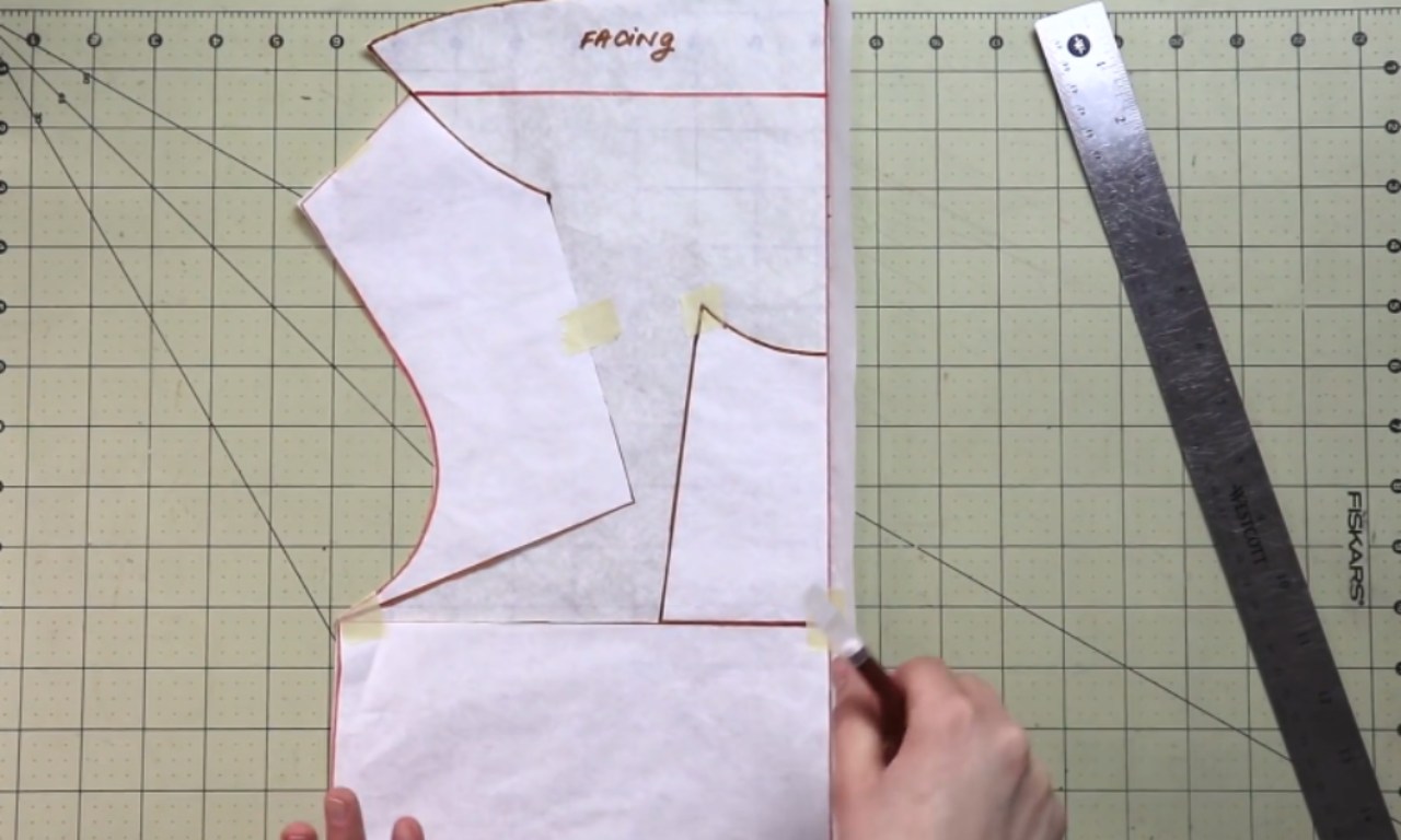 A person uses a craft knife to trim a paper sewing pattern on a gridded cutting mat.