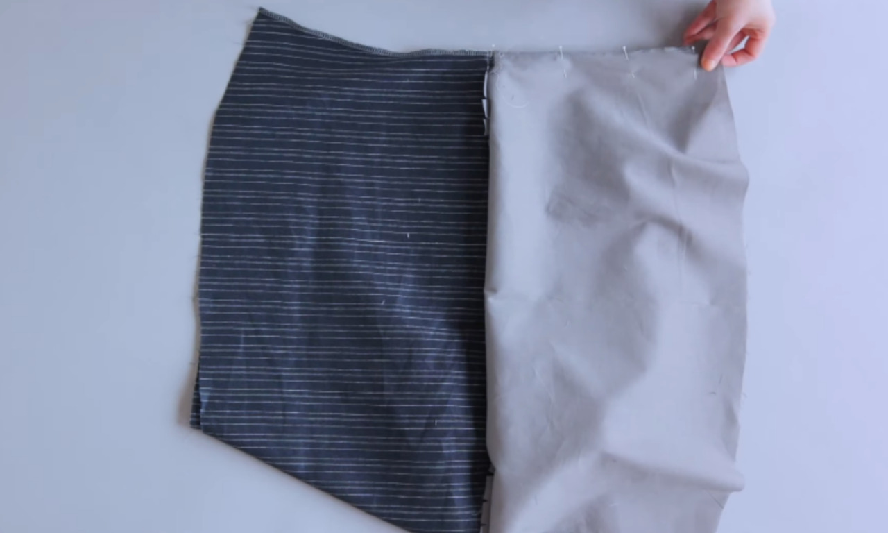 A sewer pinning the shoulder seams of the pinstripe main fabric and the solid grey lining for a lined top, the first step in the burrito sewing method.
