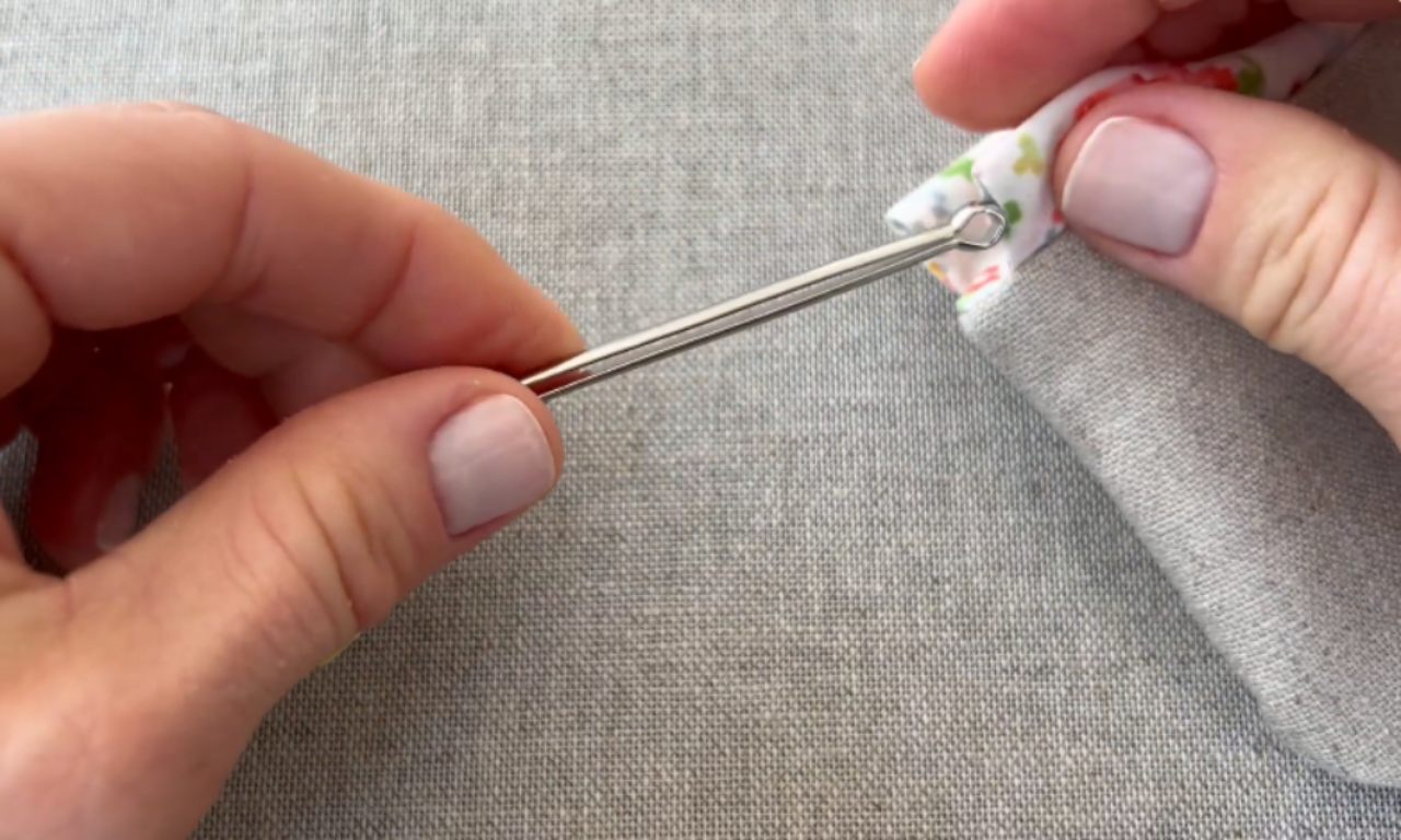 Close-up of hands using a metal bodkin to easily pull a floral fabric tie through the channel of a grey fabric casing.