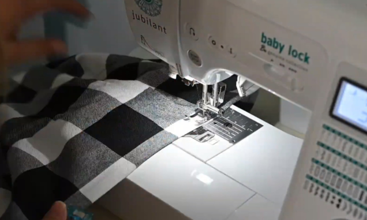 A close-up of a white Baby Lock sewing machine stitching the curved line for a scalloped hem onto a black-and-white buffalo plaid skirt.