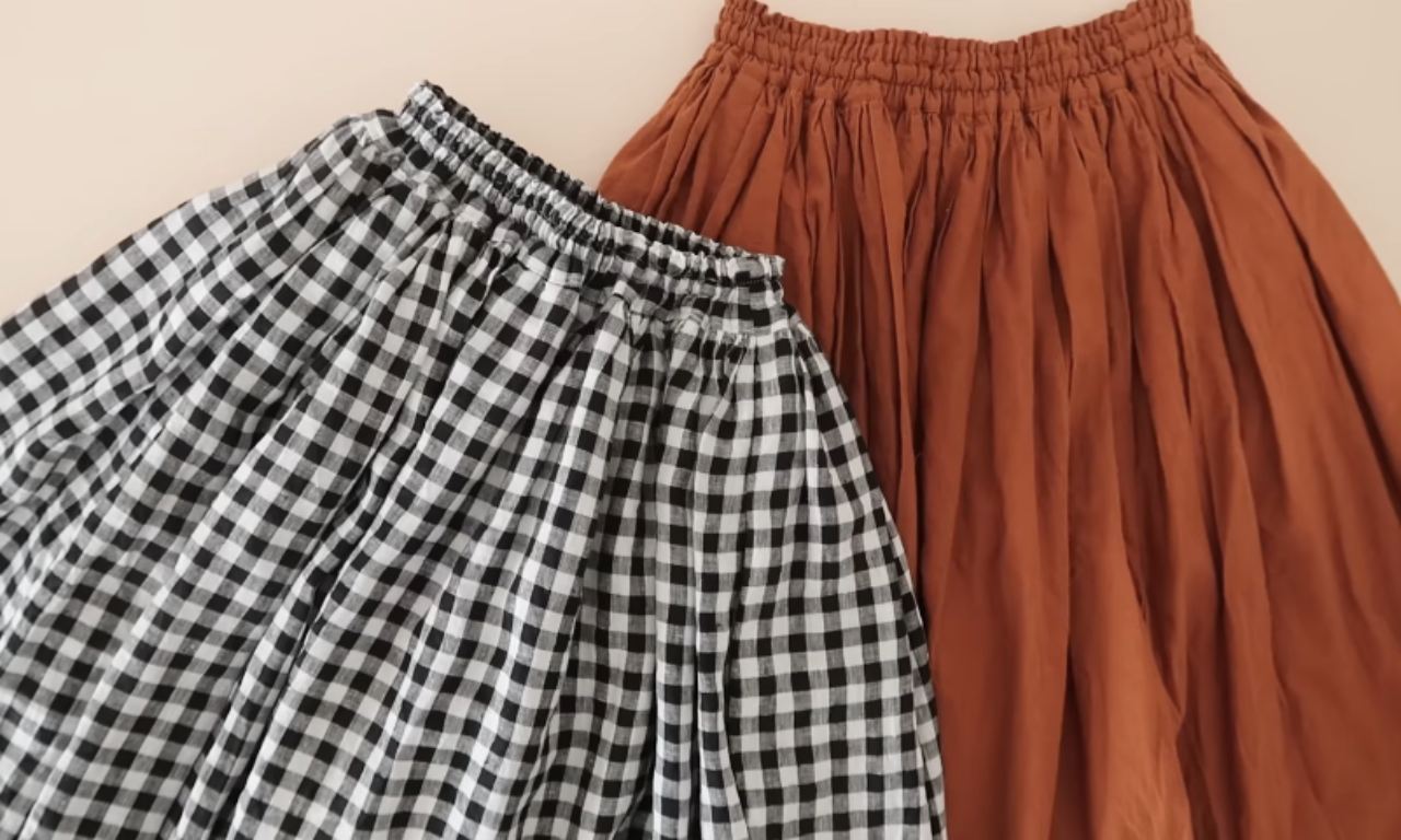 A close-up of two skirts with gathered elastic waists. One skirt has a black and white gingham pattern, and the other is a solid rust-brown.