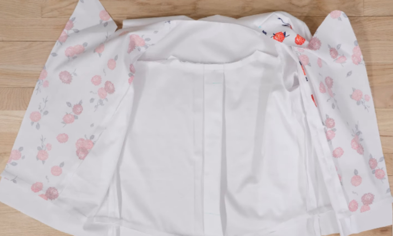 A floral-print jacket laid face down and open on a wood floor, revealing its solid white lining.
