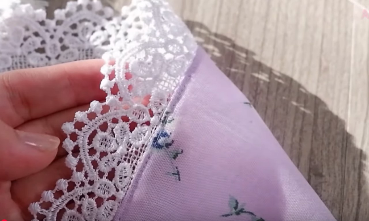 A sewer's hands carefully guiding white eyelet lace fabric through a sewing machine to stitch a French seam.
