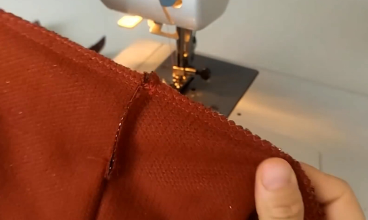 A close-up of a pressed-open seam on a piece of burnt orange fabric. The raw edges of the seam allowance have been neatly finished with a serger stitch.