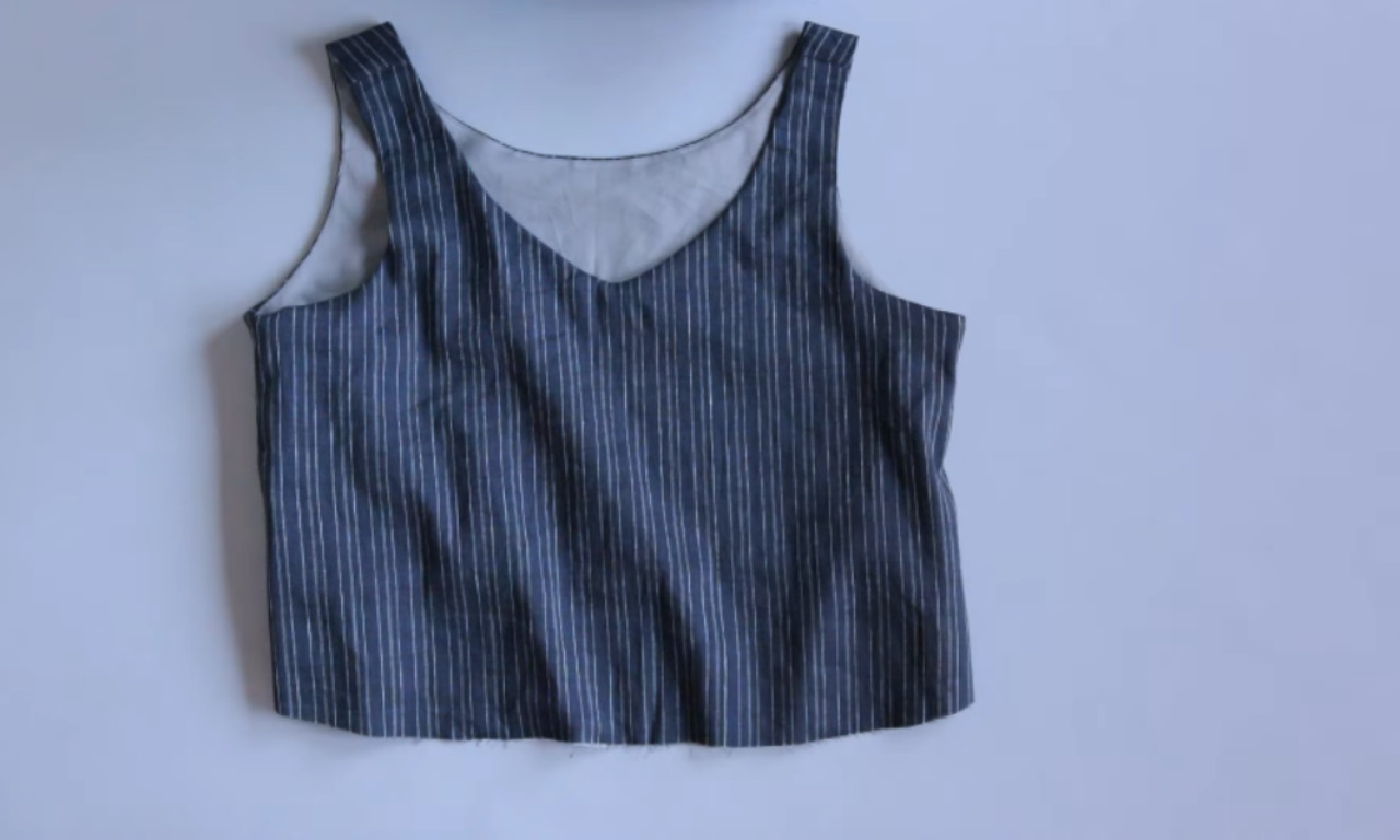 A blue and white pinstripe sleeveless top laid flat, showing the perfectly clean, finished neckline and armholes created by the burrito sewing method.