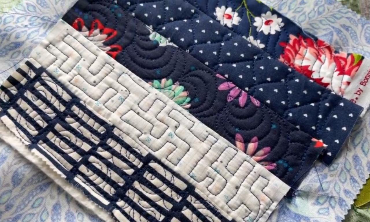 A quilted block made from diagonal strips of scrap fabric in blue and white patterns. Each strip showcases a different free motion quilting design, including a maze pattern and scallops, as a practice example.