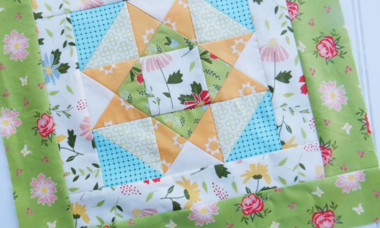 A close-up of a colorful star quilt block made with yellow, blue, and green floral fabrics. The block is framed by a perfectly flat, bright green floral border, demonstrating the correct technique for adding borders to a quilt.