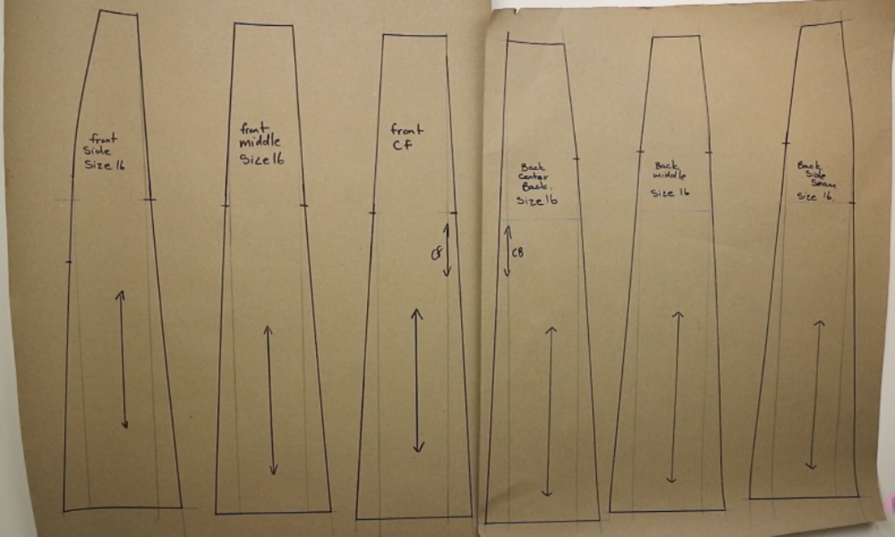 A hand-drafted paper sewing pattern for a six-panel skirt. The six long, flared panel pieces are laid out on brown paper, each labeled with its position and marked with a grainline arrow.