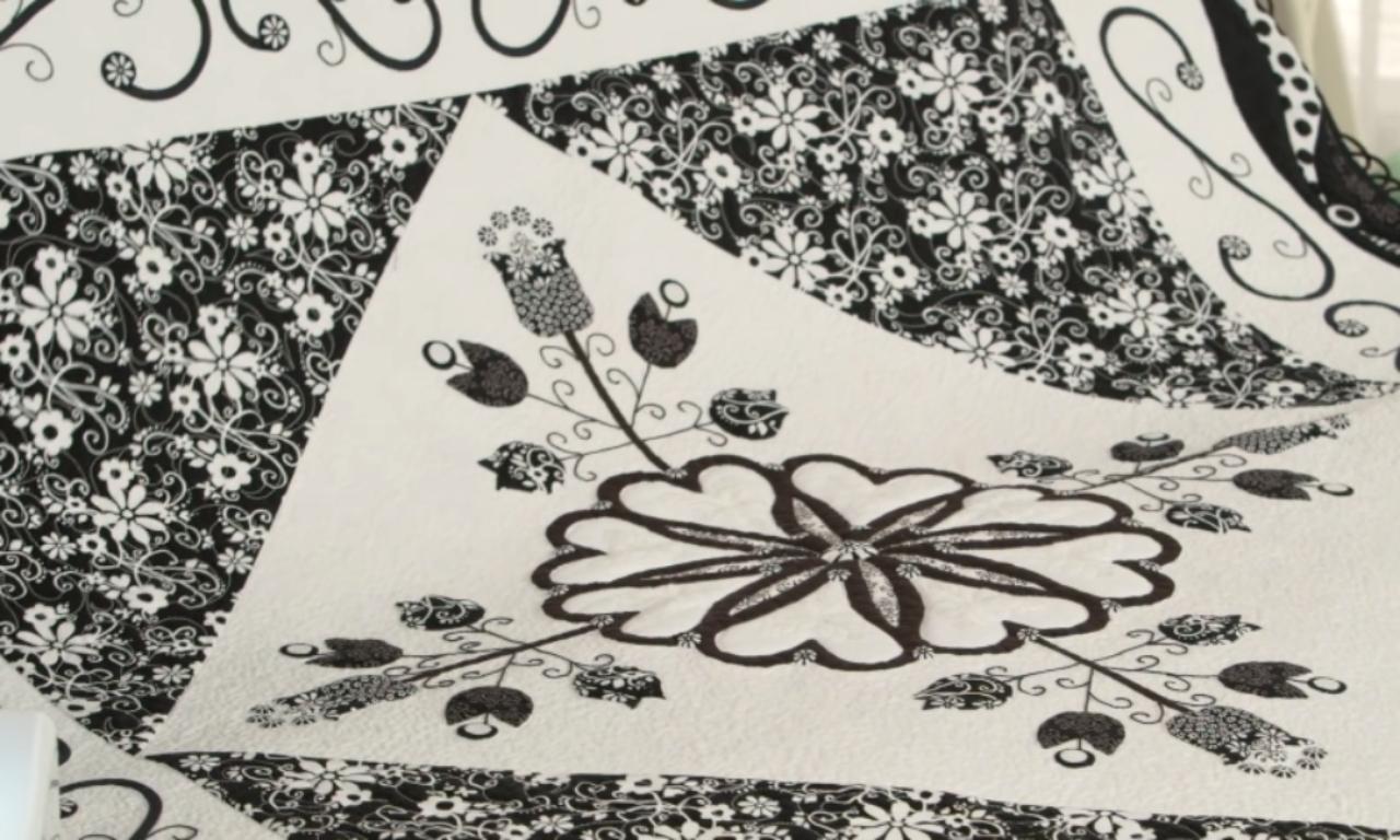 a black and white quilt featuring a large, appliquéd flower surrounded by contrasting floral and scroll patterns.