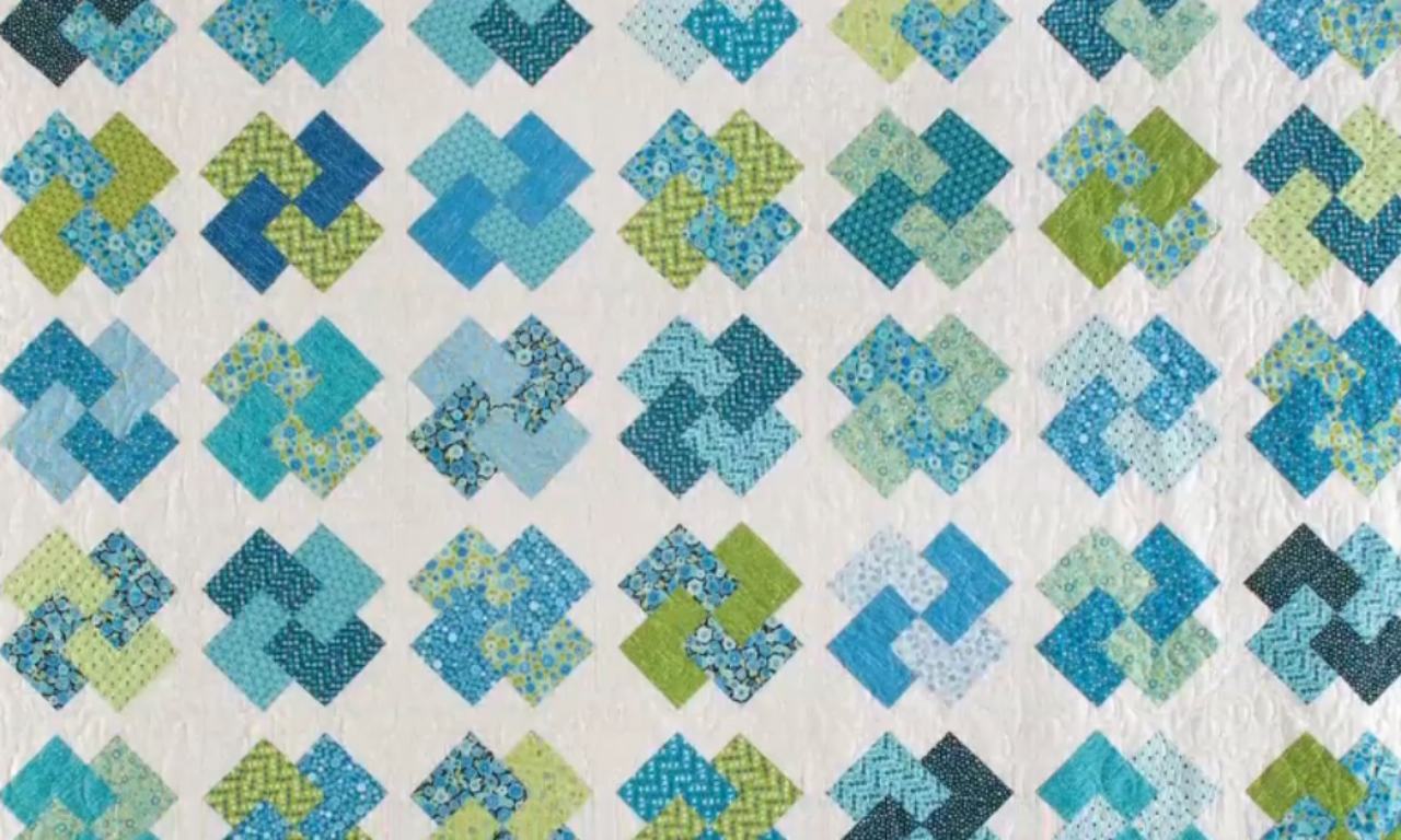 A finished Glad All Over quilt showing the woven block pattern in various shades of blue, green, and teal, set on a white, textured background.