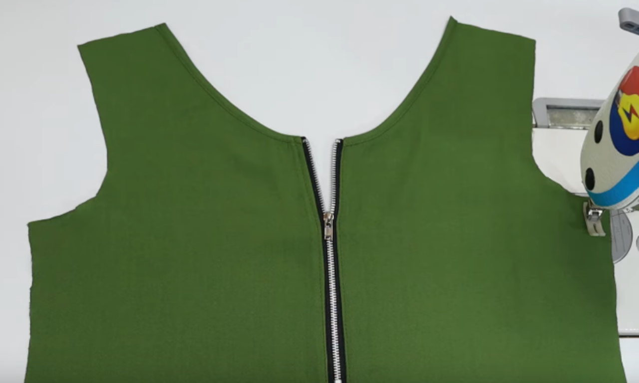 A close-up of a finished center front zipper neatly installed in a green sleeveless top, showing clean, professional stitching.