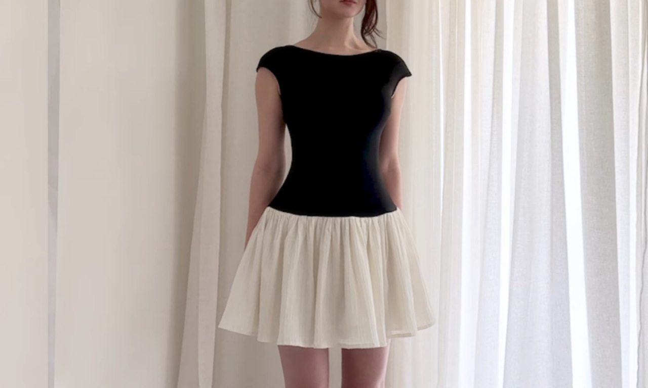 A woman modeling a finished DIY drop-waist dress with a fitted black boat-neck bodice and a short, gathered cream-colored skirt.