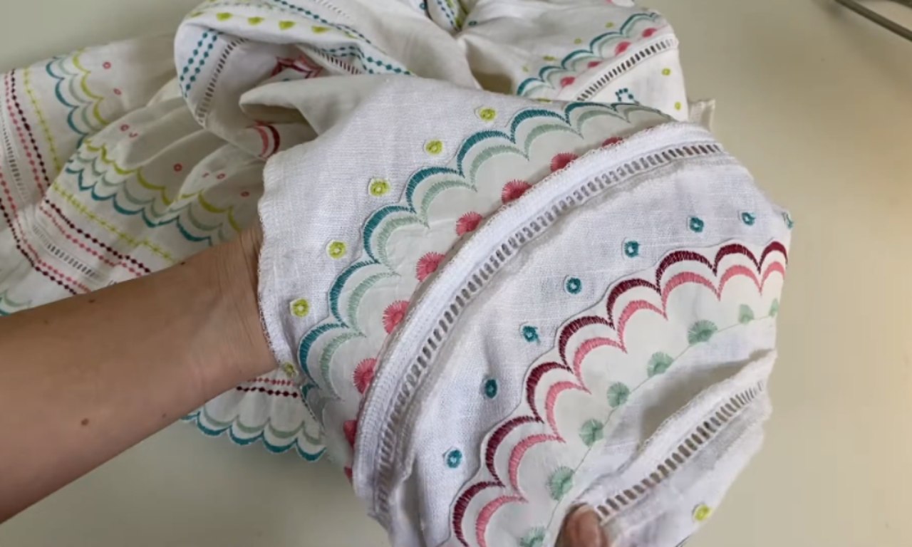 A close-up of a white linen garment featuring colorful decorative stitches in scalloped patterns of teal, pink, and green, demonstrating creative sewing machine embroidery on a sleeve hem.