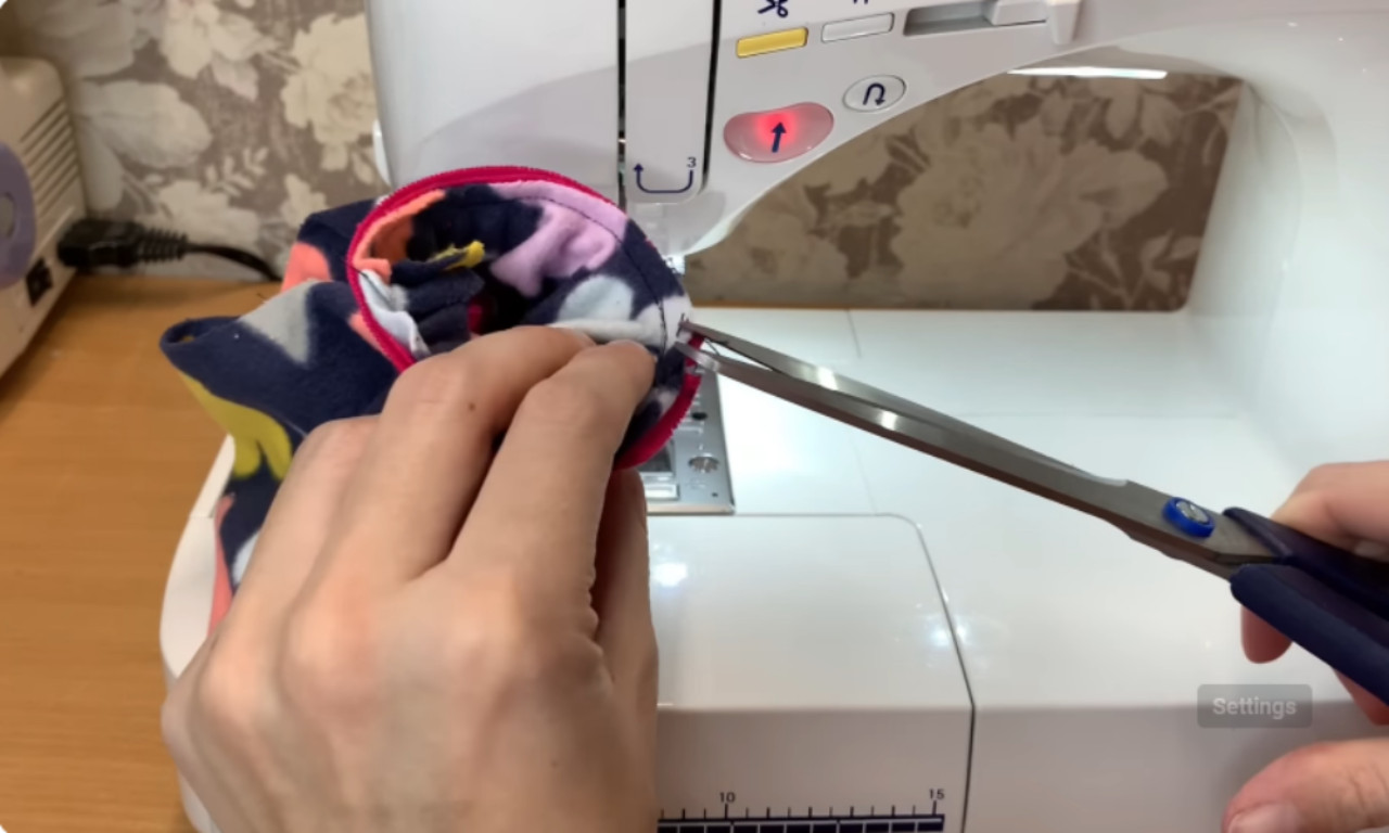 A close-up of hands sewing the pink trim on a dog shirt with a sewing machine and using small scissors to snip the thread.