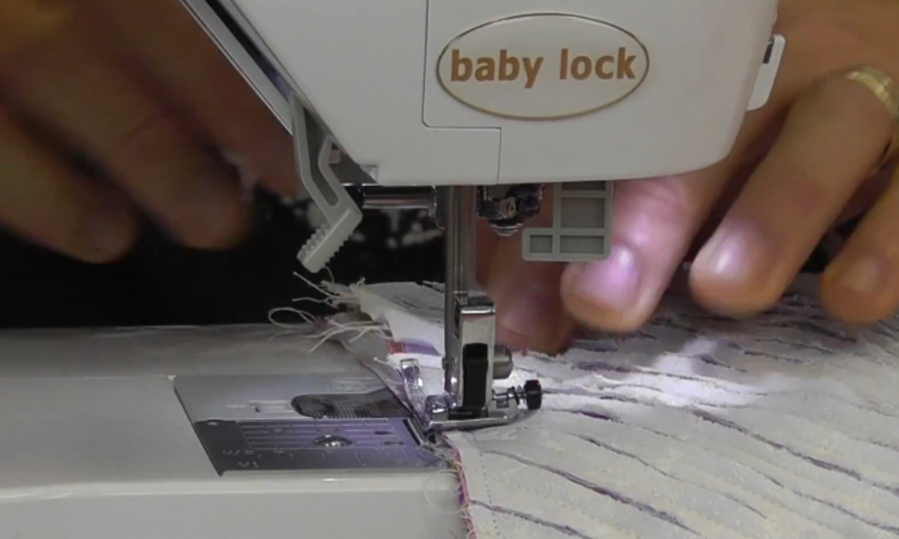 A close-up of a Baby Lock sewing machine stitching the seam of a chenille quilt block, with hands guiding the fabric under the presser foot.