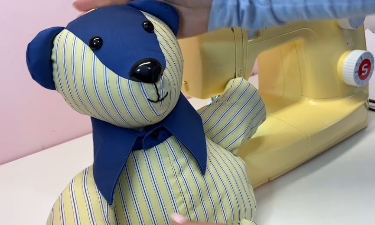 A finished memory bear made from a blue and yellow striped shirt, with a sewing machine visible in the background.