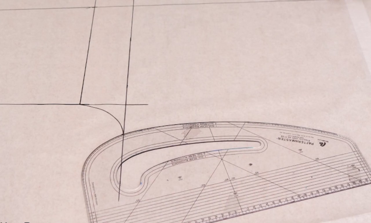 A close-up of a clear pattern master ruler being used to draw the crotch curve on a paper sewing pattern for the halter neck jumpsuit.