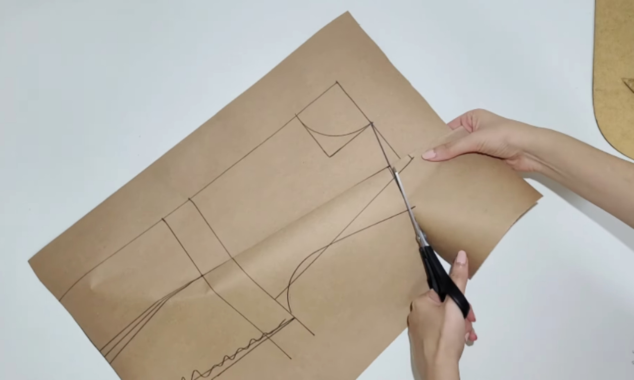 A person cutting a paper pattern along drawn lines with scissors, showing the back piece of a garment draft.