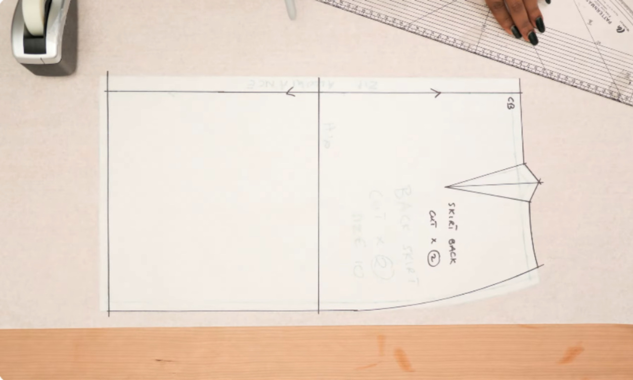 A person drafting the basic back skirt pattern on white paper before adding the vent extension.